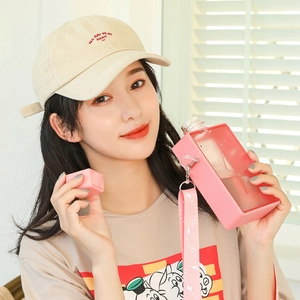 Pink rectangular plastic water bottle with adjustable strap shown with a beige baseball cap
