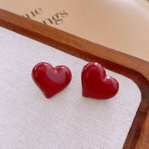 Macro shot of red heart stud earrings with glossy enamel on light linen background