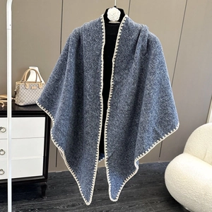 Blue-grey knitted shawl poncho with white jagged edges displayed on a hanger