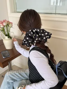 Polka dot satin scrunchie with pearls shown on braided hair in a cozy indoor setting