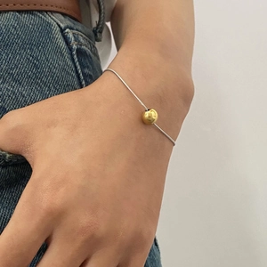 Close-up of minimalist silver snake chain bracelet featuring a single gold bead on wrist