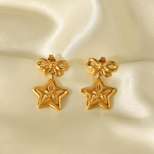 Detail of 18k gold butterfly bow earrings with star pendants on silk background