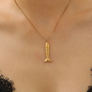 Close-up of golden fish pendant with detailed scales on a fine chain worn by a model