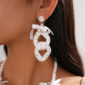 Close-up of oversized white acrylic chain earrings with blue ink spots and pearl bow detail