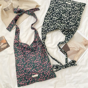 Detail of floral canvas shoulder bags with knotted bow straps on a rustic white background