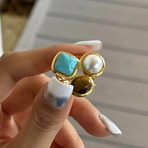 Gros plan détaillé d'une bague dorée ornée de turquoise, perle et oeil de tigre