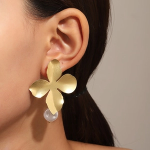 Détail d'une boucle d'oreille fleur en or mat avec perle blanche sur un mannequin