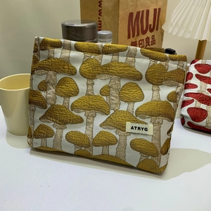 Detail view of the yellow mushroom pattern on fabric cosmetic bag with brand label