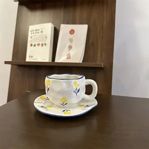 Detail of hand-painted floral ceramic coffee cup with irregular wavy textures on wood table