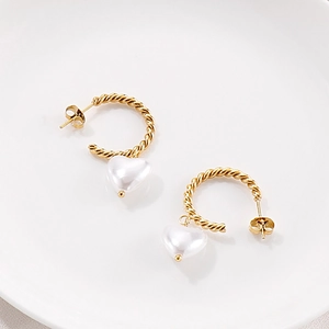 Détail de créoles dorées torsadées en C avec pendentifs en perles blanches en cœur