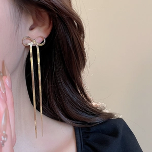 Close-up of golden bow long tassel earrings on model showing elegant drape and length