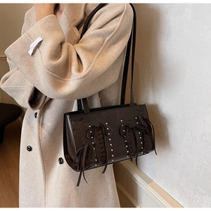 Detail of dark brown PU leather shoulder bag with cross lace-up tassels and silver rivets