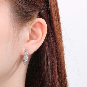 Close-up of a silver C-shaped stainless steel earring with pavé-set zircons on a model