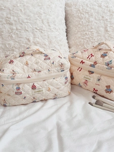 Quilted beige cosmetic bag set with bear and rabbit prints on a soft bed background