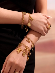 Close-up of gold layered chain bracelets with coin and 3D initial letter charms