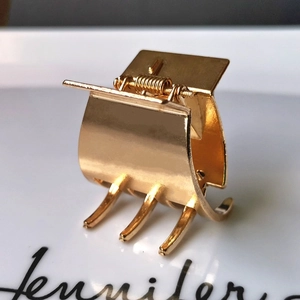 Macro shot of a minimalist gold metal hair claw clip reflecting on a white surface