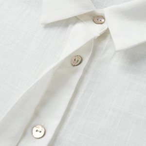 Gros plan sur un tissu en lin blanc avec trois boutons en nacre irisante sur une chemise