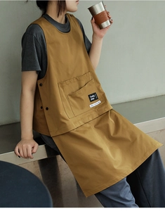 Detail of a brown work apron with large front pockets and stitched brand labels