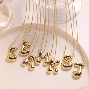 Detail of 18K gold plated puffed initial necklaces in a stylish ceramic dish