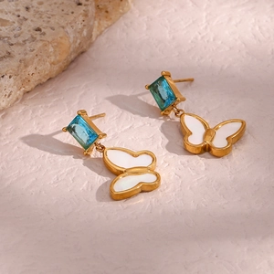 Detail of gold butterfly drop earrings with a blue square zircon and shell wings
