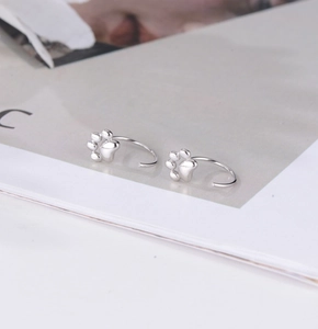 Detail of silver cat paw earrings placed on a magazine with soft natural lighting