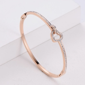 Rose gold heart bangle with pavé crystals and open cutout design on white pedestal
