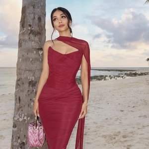 Detail of elegant dark red ruched bodycon dress with sequin bag against a sunset beach backdrop