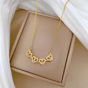 Detail of gold titanium steel clover necklace with crystal heart pendants on beige box