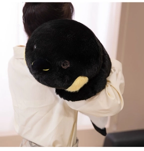 Détail d'une grande peluche pingouin tenue par un adulte montrant sa taille et sa texture douce