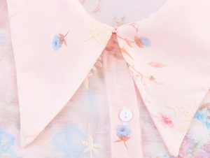 Close-up of floral embroidery and print on pink shirt collar with button detail