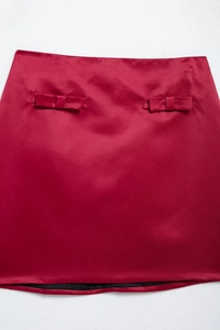 Detail of burgundy satin mini skirt with elegant decorative bows and glossy silk texture