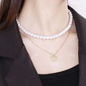 Detail of a layered necklace featuring a white pearl choker and a gold heart pendant