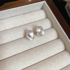 Macro shot of silver brushed metal C-shaped stud earrings in a soft velvet jewelry box