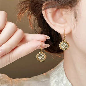 Close-up of vintage flower earrings with green accents worn by a model in soft light