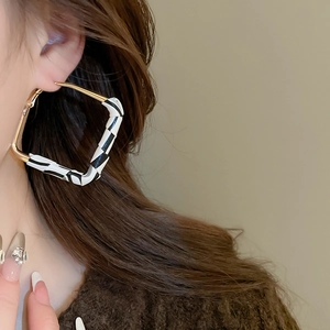 Macro view of gold metal square hoop earring with black and white woven texture on model