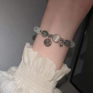 Detail eines Perlenarmbands aus Katzenaugenstein mit Fu-Anhänger und Glöckchen