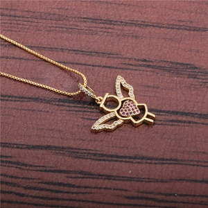Close-up of golden angel heart pendant with pink crystals on dark wooden surface