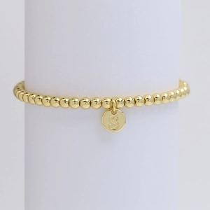 Detail shot of golden beaded bracelet with polished round letter S pendant on a display