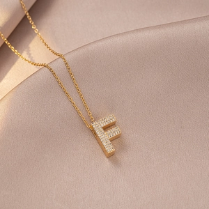 Detailed close-up of golden letter F necklace pendant with pavé set white zircon stones