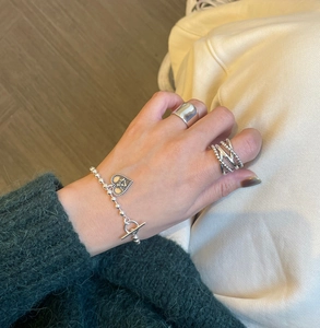 S925 silver rings and heart pendant bracelet worn over green knit sweater