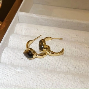 Close-up of gold C-shaped earrings with faux tiger eye stones in a white velvet box