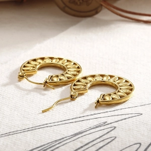 Macro detail of golden C-shaped hoop earrings featuring intricate leaf relief patterns