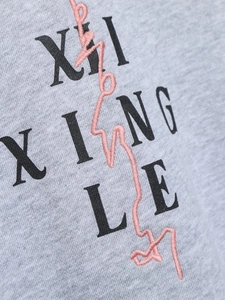 Gros plan sur tissu gris texturé avec lettrage XING LE et broderie rose détaillée