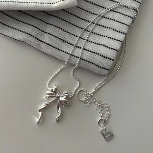 Minimalist 925 sterling silver bow pendant necklace on a striped fabric background