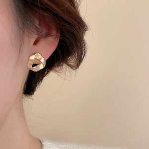 Detail of elegant matte gold irregular triangular earring on model for luxury style