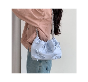 Detail of light blue PU leather shoulder bag with decorative bows and silver chain strap