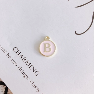 Detail of pink enamel round alloy charm with golden letter B for DIY necklace