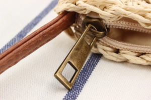 Detail of bronze metal zipper and brown leather strap on a beige woven paper straw bag
