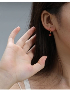Close-up of gold-plated hoop earrings featuring a brilliant round-cut red gemstone on model