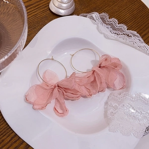 Dettaglio di orecchini a cerchio con fiori in tessuto rosa su piatto di pizzo